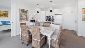 A modern kitchen with white cabinets, a dining table with wicker chairs, and pendant lighting. - A taste of paradise in inner city suburbia (Maribyrnong)