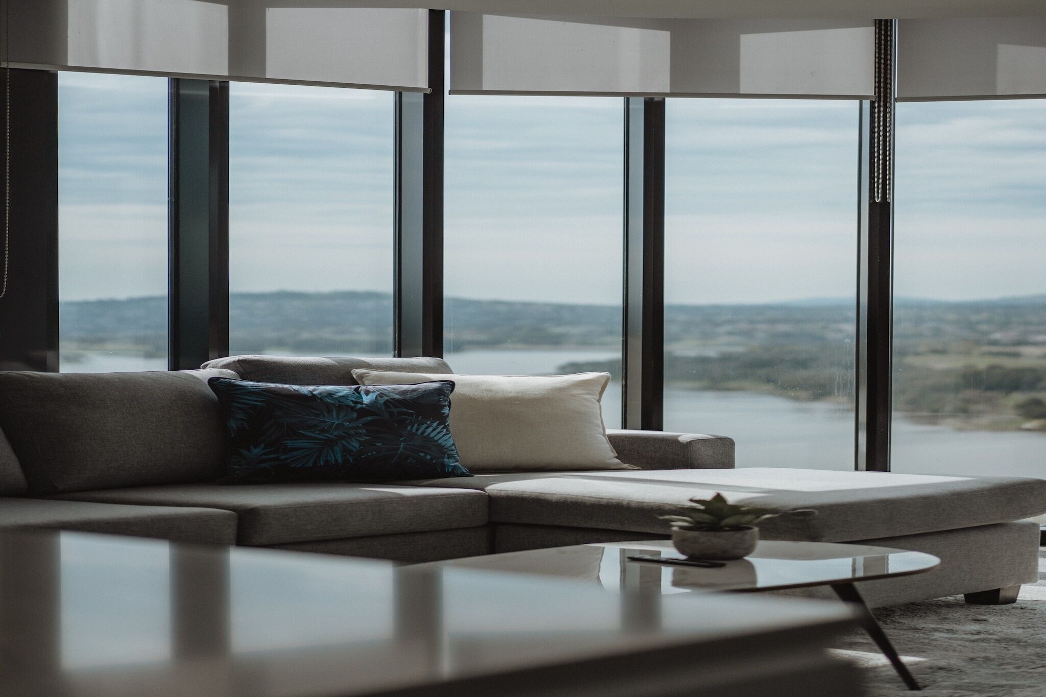 A modern living room with a sectional sofa, a coffee table, and large windows offering a view of a landscape.