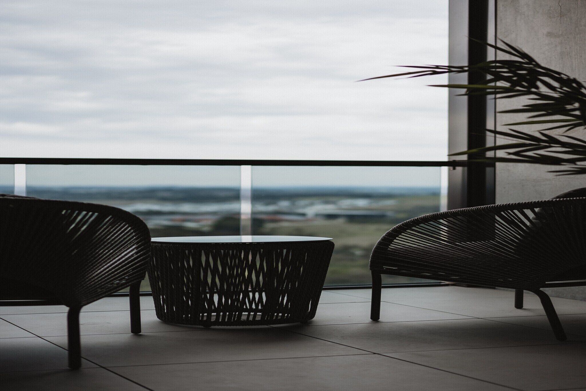 A balcony with two wicker chairs and a round table, overlooking a distant landscape.