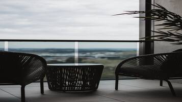 A balcony with two wicker chairs and a round table, overlooking a distant landscape.