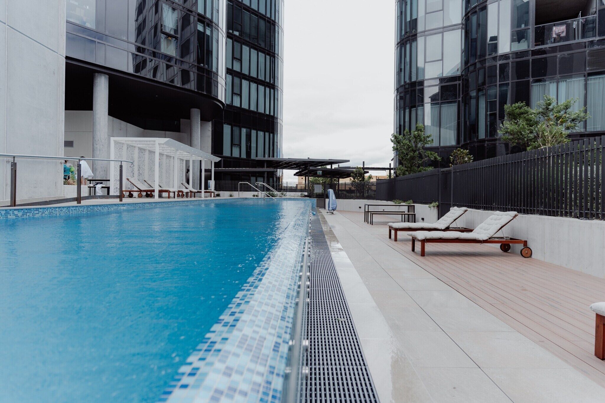 A swimming pool with lounge chairs, a covered seating area, and modern buildings in the background.