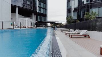 A swimming pool with lounge chairs, a covered seating area, and modern buildings in the background.
