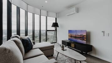 Un salon moderne doté d’une grande fenêtre, d’un téléviseur à écran plat, d’un canapé, d’une table basse et d’un lampadaire.