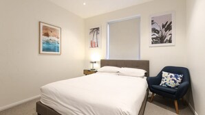 Un dormitorio con cama, mesita de noche, una silla y decoración en la pared.