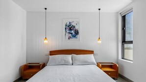 A modern hotel room with a large bed, two bedside tables, a window, and a wall-mounted abstract painting. - Vibrant 2-Bed Apartment Near St Kilda Beach (St Kilda)