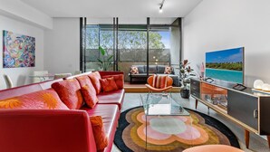 A modern living room with a red sofa, a glass coffee table, and a TV on a cabinet. - Vibrant 2-Bed Apartment Near St Kilda Beach (St Kilda)