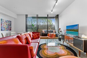 Ein modernes Wohnzimmer mit einem roten Sofa, einem Glastisch und einem Fernseher auf einem Schrank.