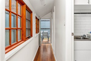 Un passadís estret amb finestres de fusta, una zona de cuina amb un rentamés i vista a una zona d'estar exterior.