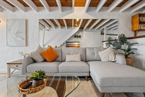 A modern living room with a sectional sofa, a glass coffee table, and a staircase leading to an upper level. - Chic 2-Bed Cabin-Style Home by Mooloolaba Beach (Mooloolaba)