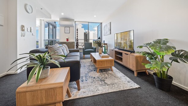 Uma sala de estar moderna com sofá, mesa de centro, televisão e plantas em vasos.