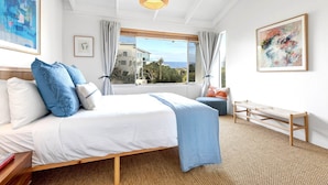 Una habitación de hotel con una cama, una ventana con cortinas, un banco y obras de arte en las paredes.