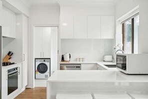 Una cocina moderna con armarios blancos, lavadora integrada, microondas y cafetera.