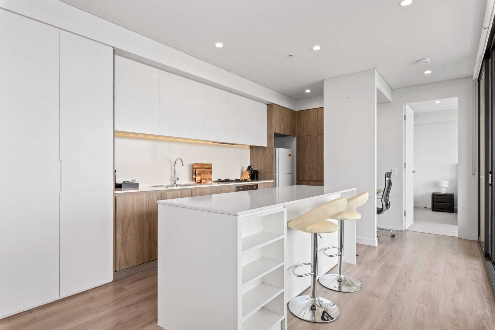 A modern kitchen with white cabinetry, a central island, and bar stools.