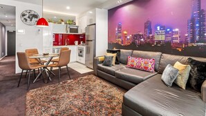 Una sala de estar moderna con un mural de la ciudad, un comedor con pared de acento roja y una cocina con armarios blancos.