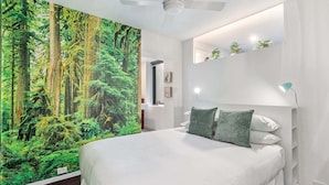 Un dormitorio con una cama grande, un mural en la pared con un bosque, un ventilador de techo y una mesita de noche con lámpara.