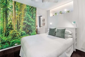 A bedroom with a large bed, a wall mural of a forest, a ceiling fan, and a bedside table with a lamp. - Sleek & Central 2-Bed Apartment in Melbourne (Melbourne)