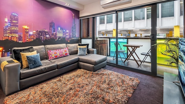 Una sala de estar moderna con un sofá seccional grande, un mural con vista a la ciudad y un balcón con vista a la piscina.