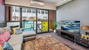 Una sala de estar moderna con un sofá, televisor y vistas a un balcón con mobiliario exterior.