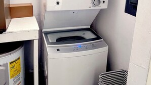 Un área de lavandería compacta con lavadora y secadora apiladas, un mueble pequeño y un bote de basura.