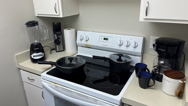 Una cocina con estufa, ollas, cafetera y licuadora.