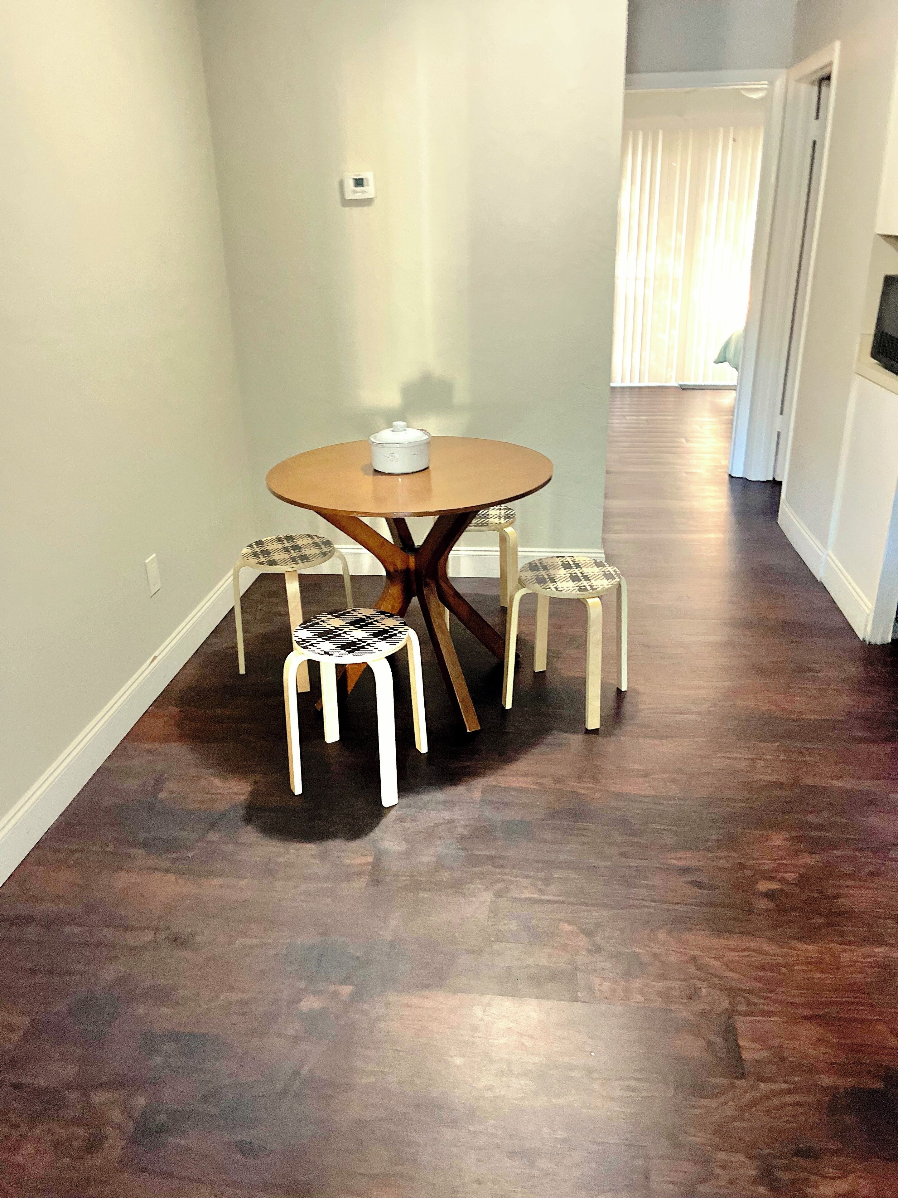 A hallway with a round table and two chairs, a thermostat on the wall, and a door leading to another room.