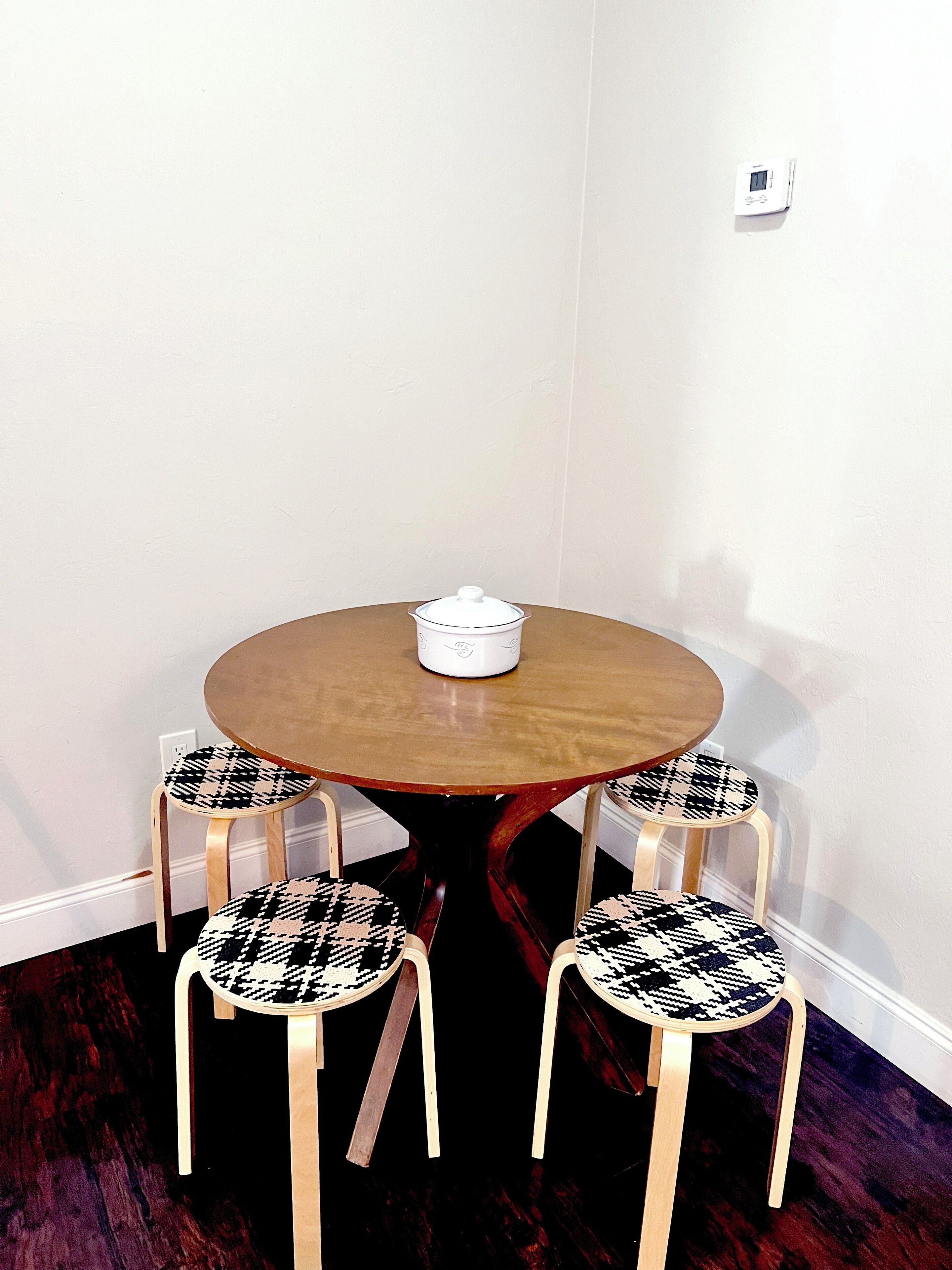 A round wooden table with a white object on top, surrounded by four black and white patterned chairs.