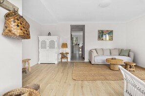 Ein Wohnzimmer mit einer Couch, einem weißen Schrank, einem Korbwannenstuhl, einer Lampe und einem Bild an der Wand.