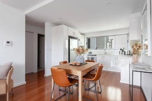 A modern kitchen with white cabinets, a dining table with chairs, and a small island with a sink. - Bright 2-Bed Apartment with Balcony & Garage (Five Dock)