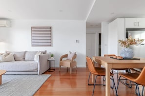 A modern living room with a sofa, a small table, a chair, a dining table with chairs, and a kitchen area with cabinets. - Bright 2-Bed Apartment with Balcony & Garage (Five Dock)