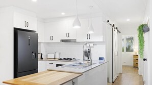 Una cocina moderna con armarios blancos, un refrigerador negro, luces colgantes, una isla de madera y vistas a un pasillo con una planta.