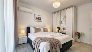 Una camera d'albergo con un letto, comodini, un condizionatore d'aria, un lampadario, uno specchio e un vaso con fiori.