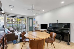 Ein modernes Wohnzimmer mit Klavier, Fernseher und Essbereich mit Stühlen und Tisch.