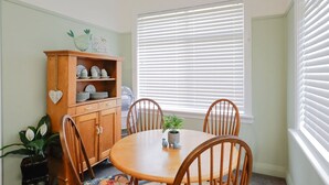 A dining area with a wooden table, chairs, a cabinet with dishes, and a window with blinds.