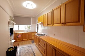 A kitchen with wooden cabinets, a gas stove, and a window. - Cosy Sun-Filled Cottage (Tenterfield)