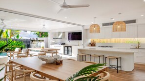 Una cocina moderna con armarios blancos, una isla central y un comedor con mobiliario de madera.