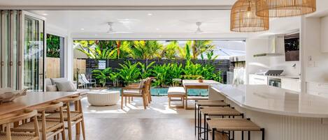 A modern kitchen with a bar area, a pool, and a lush garden view.