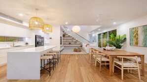 Eine moderne Küche mit einer zentralen Kochinsel, Holzböden und einer Treppe, die in einen Wohnbereich mit Esstisch und Stühlen führt.