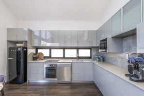A modern kitchen with grey cabinets, a dishwasher, an oven, a sink, and a coffee machine. - Fun for Families: Location, Cinema, Games, Wifi (Leederville)