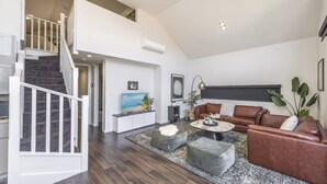 A spacious living area with a staircase, a flat-screen TV, a brown leather sofa, and a coffee table. - Fun for Families: Location, Cinema, Games, Wifi (Leederville)