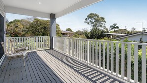 Une terrasse en bois avec une balustrade blanche, un banc et une vue sur la verdure et les maisons environnantes.