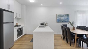 Une cuisine moderne avec un îlot central, un coin repas avec une table et des chaises en bois, et un tableau accroché au mur.