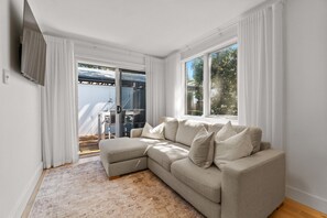 A living room with a sectional sofa, a flat-screen TV mounted on the wall, and a sliding glass door leading to an outdoor area. - Stylish 2-Bed Townhouse in Leafy Hyde Park (Hyde Park)