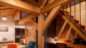 Ein geräumiger Wohnbereich mit einer Holztreppe, einem Sofa, einem blauen Sessel und einem Esstisch.