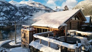 Eine Holzlodge mit verschneitem Dach, einer Steinsäule und Blick auf schneebedeckte Berge.