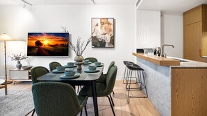 A modern dining area with a table set for four, a kitchen with a wooden countertop, and two framed artworks on the wall. - Stylish 3-Bed Townhouse in Vibrant Fitzroy (Fitzroy)