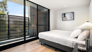 A modern bedroom with a large window, a bed, a nightstand, and a painting on the wall. - Stylish 3-Bed Townhouse in Vibrant Fitzroy (Fitzroy)