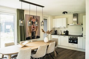 Uma cozinha moderna com armários brancos, uma mesa de jantar de madeira e luminárias pendentes.