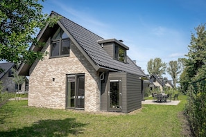 A modern house with a sloped roof, a brick facade, and a patio with outdoor furniture. - Sea View Apartment with Terrace for 8 (Elahuizen)