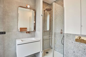 Ein modernes Badezimmer mit Duschkabine aus Glas, einem weißen Waschbecken und einem großen Spiegel.