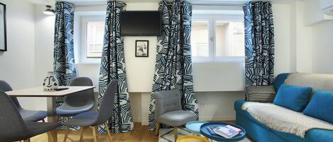 A modern living room with a blue sofa, a dining table with chairs, and patterned curtains.